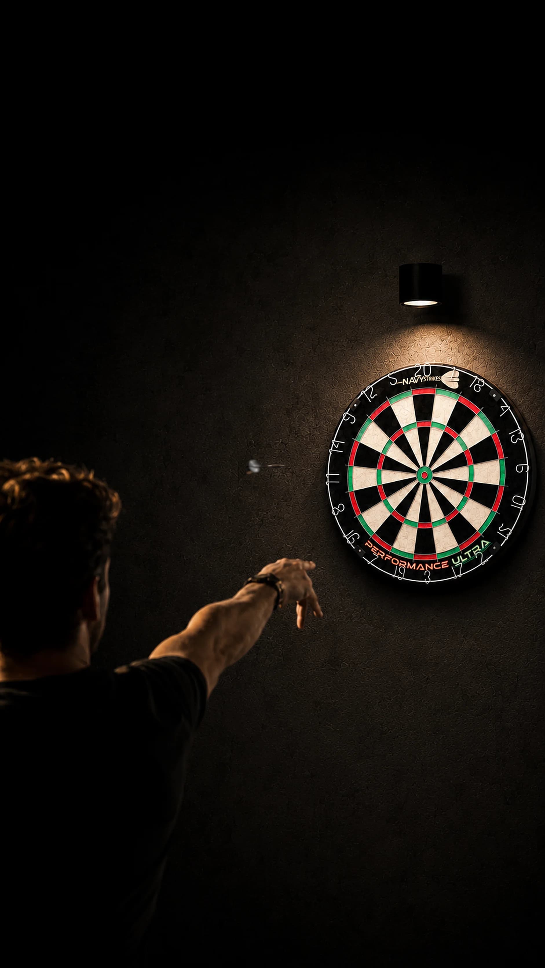Dart player throwing a dart at a Navy Strikes Performance Ultra dartboard in an atmospherically lit home setting